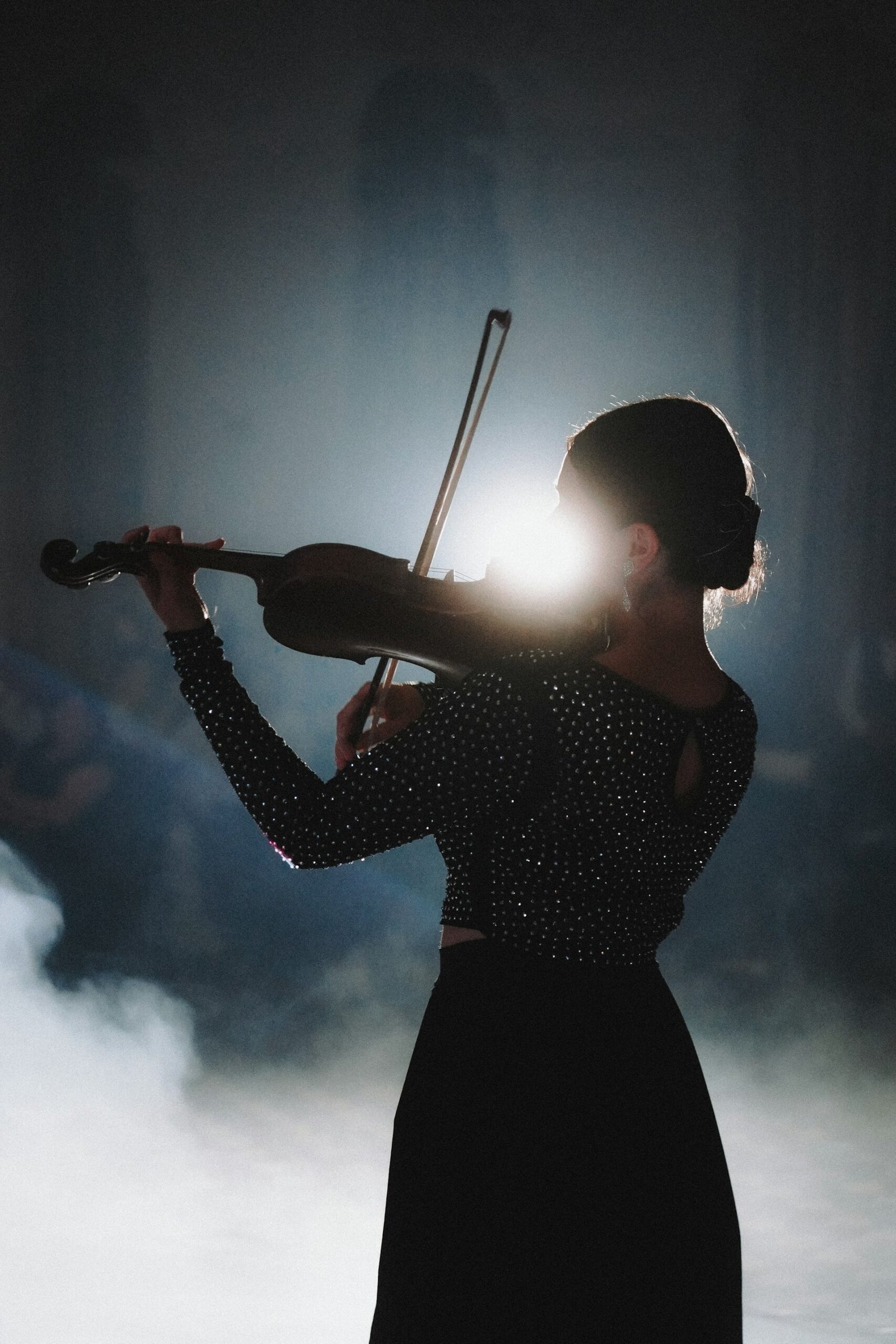 commuovere meaning — a violinist performing in dramatic spotlight and smoke, evoking the Italian art of being moved to tears by beauty