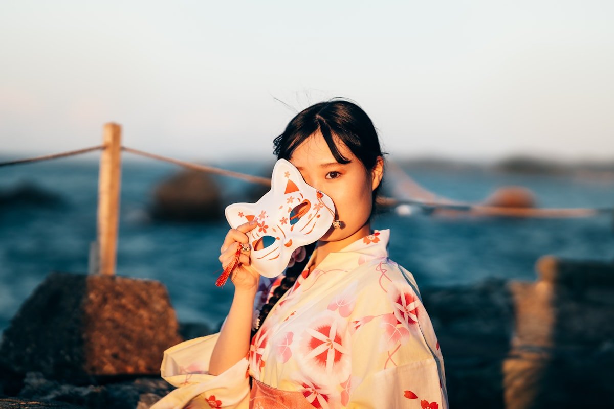 A woman in a kimono holding a traditional Japanese mask, symbolizing tatemae